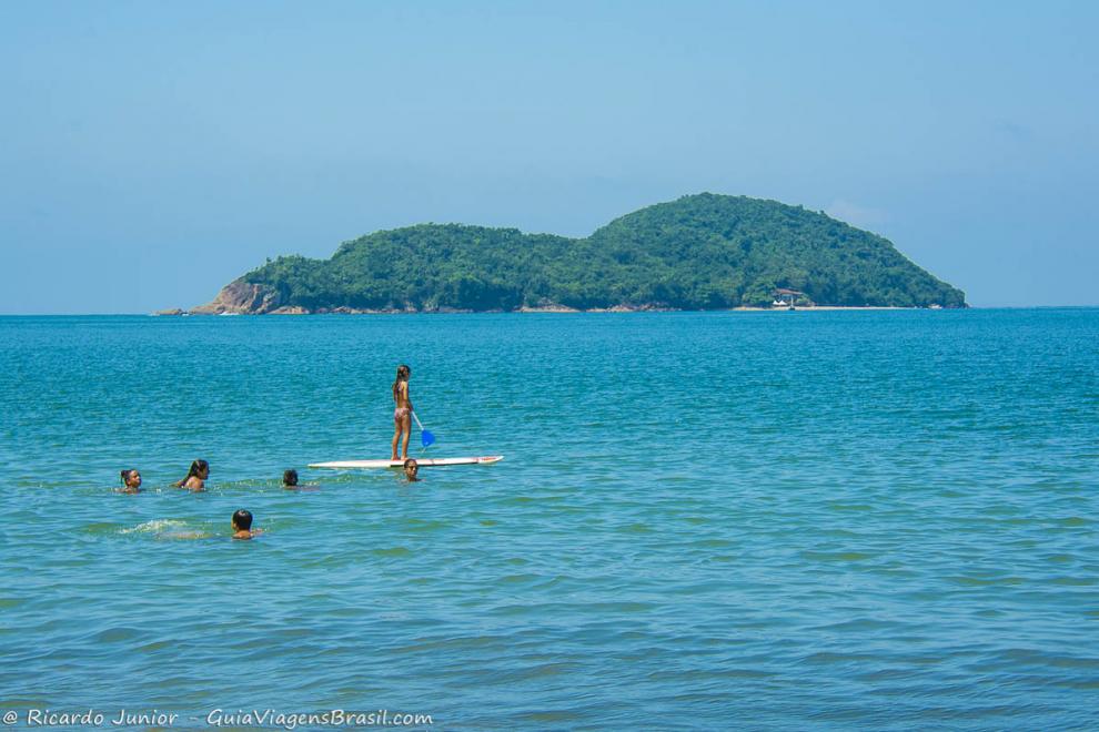 Imagem de uma menina praticando standup paddle e pessoas em volta na praia.